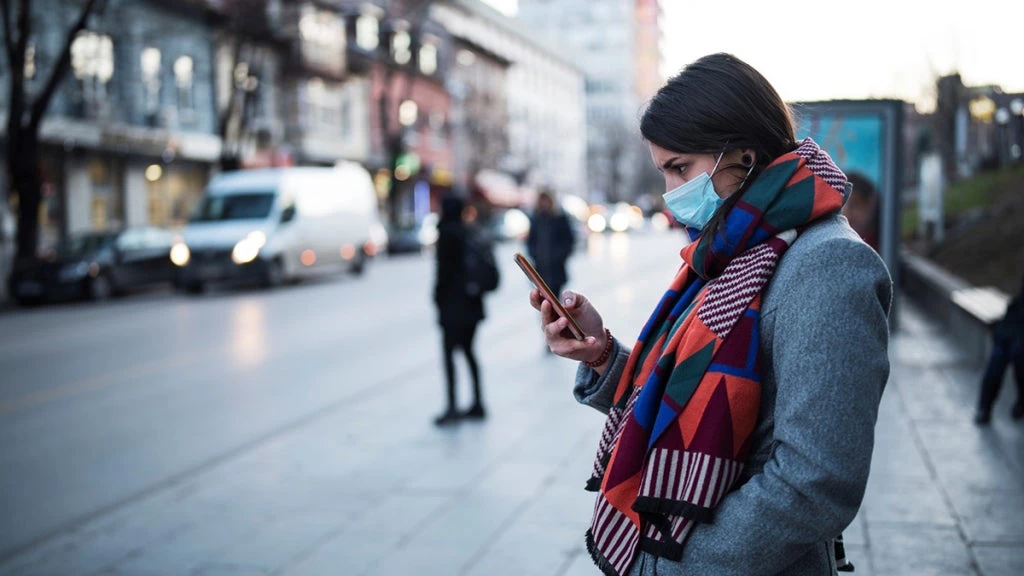 Young woman with a face mask using a smartphone. Photo: GND/iStock