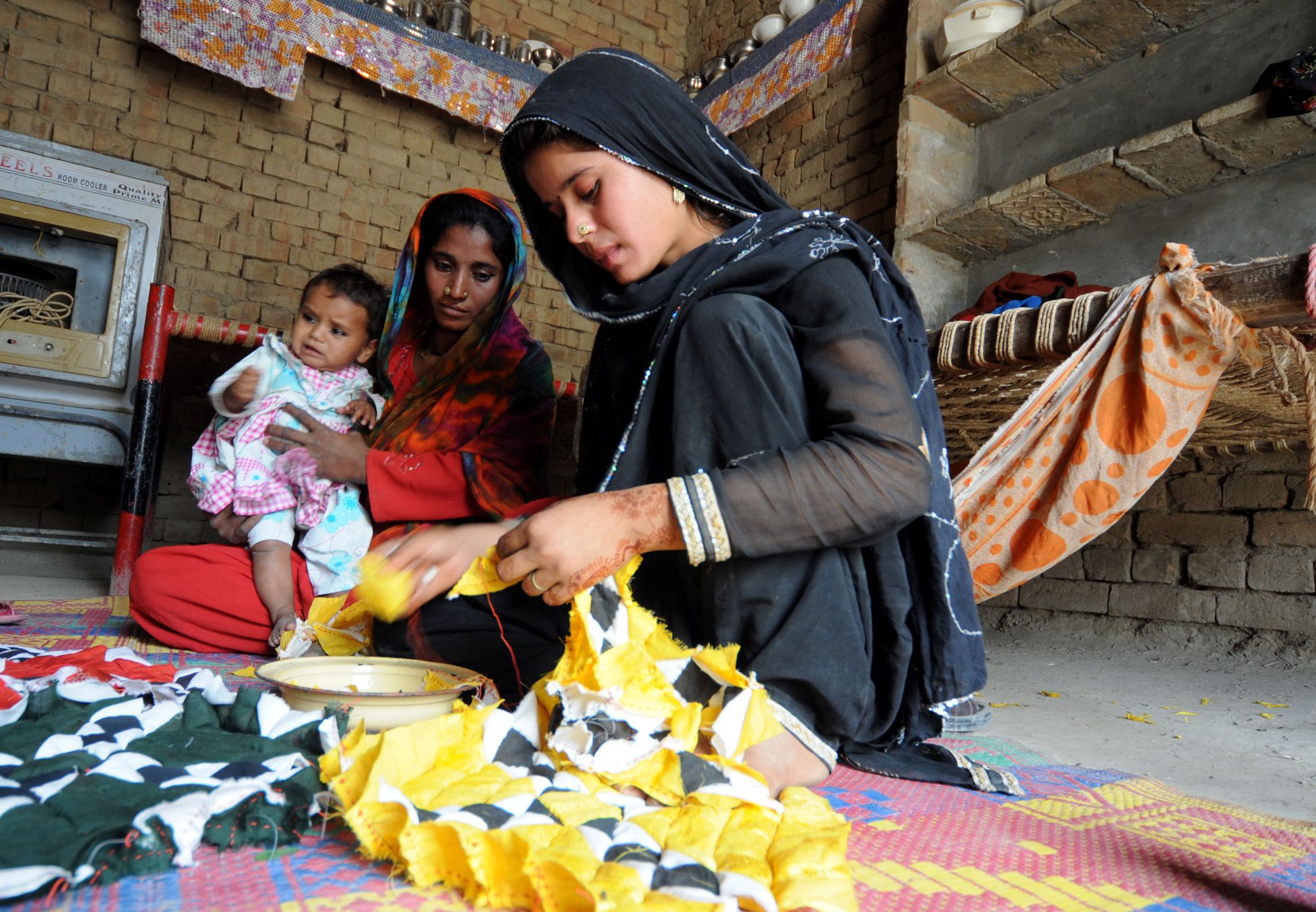 TAUNSA:PAKISTAN: Uzma Mai, elder daughter of Fida Hussain (not in the picture), stitching a RILLI or a bed cover made of small but colur-full pieces of clath as her mother Haseena Bibi with Rabia Mai (youngest daughter of Hussain) watches at Basti Sheikhan-wali near Taunsa Barrage at River Indus in Muzaffargarh District of Pakistan’s Punjab province. They are among the beneficiaries of the dam as the family have the fishing contract with authorities. The Taunsa Barrage was completed in 1958, and it has been identified as the barrage with the highest priority for rehabilitation. It requires urgent measures to avoid severe economic and social impacts on the lives of millions of poor farmers through interruption of irrigation on two million acres (8,000 km²) and drinking water in the rural areas of southern Punjab, benefiting several million farmers. Photo: Visual News Associates / World Bank