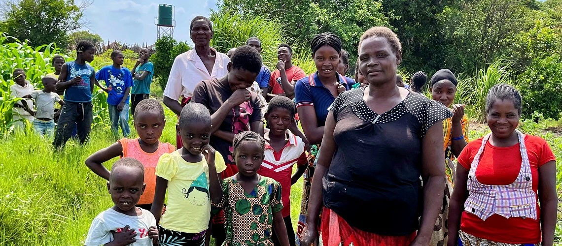 Rural community group photo with women in the front, surrounded by children in Zambia.